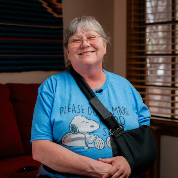 Tanya McGuire with grey hair and glasses, wearing light blue shirt with her left arm in a black sling.